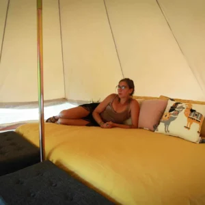 Guest relaxing on a bed inside a bell tent