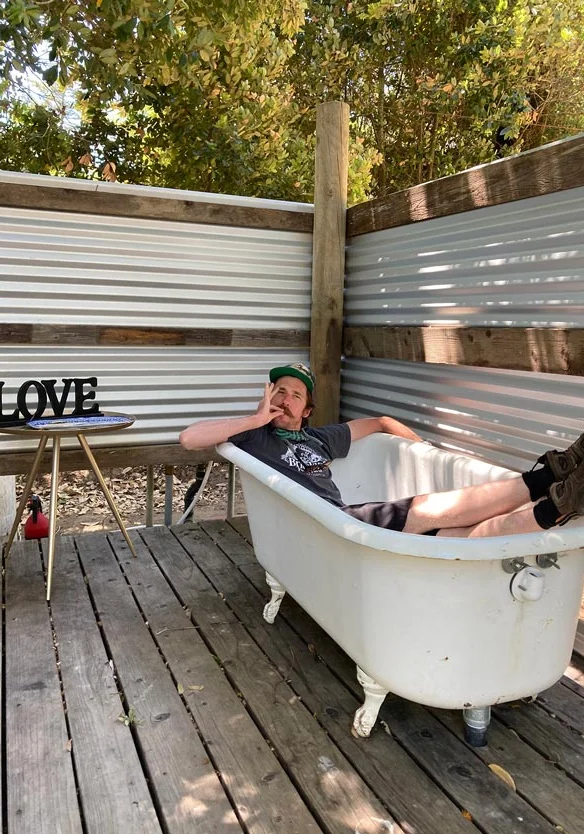 Guest relaxing in an outdoor clawfoot bathtub on a wooden deck