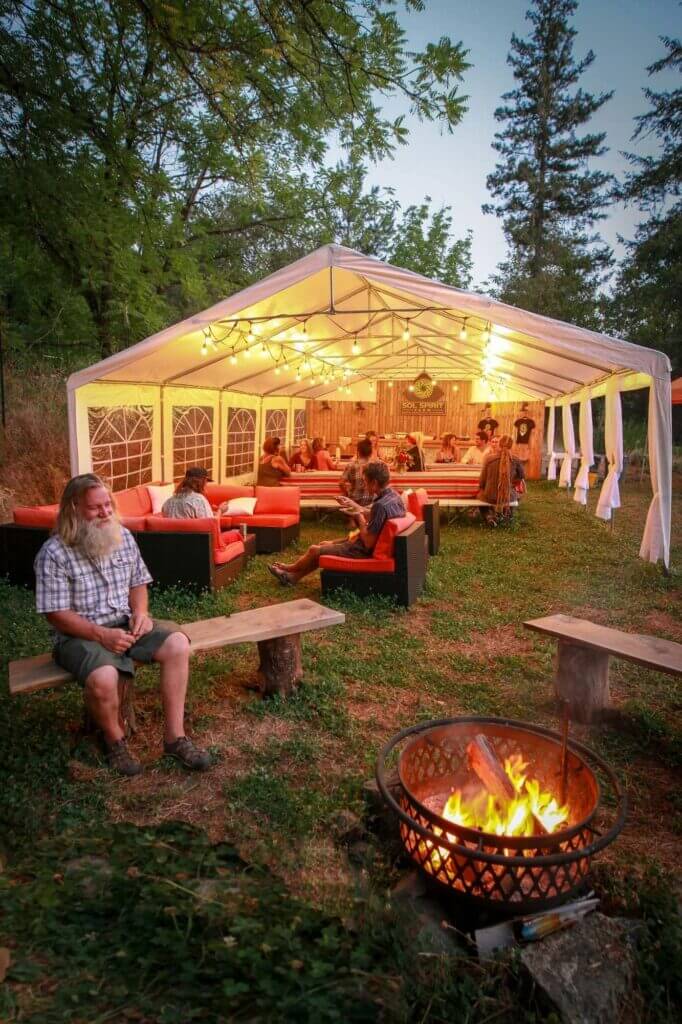 Guests gathered around a fire pit by a lit dining tent at dusk