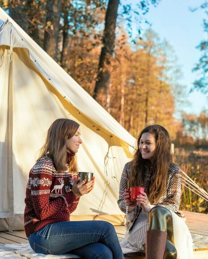 Two guests sitting with drinks in front of a bell tent